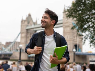 Portrait of a happy student in London holding a notebook and smiling near Tower Bridge - education concepts